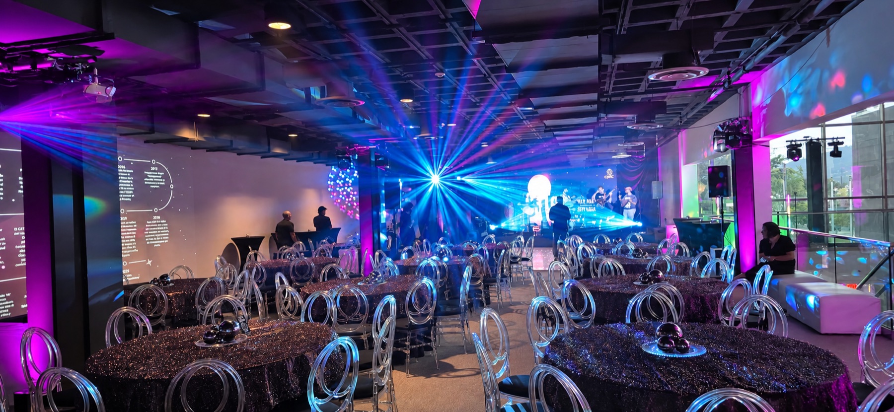 Blue and magenta beams illuminate a complete event setup with a stage, video wall and banquet seating