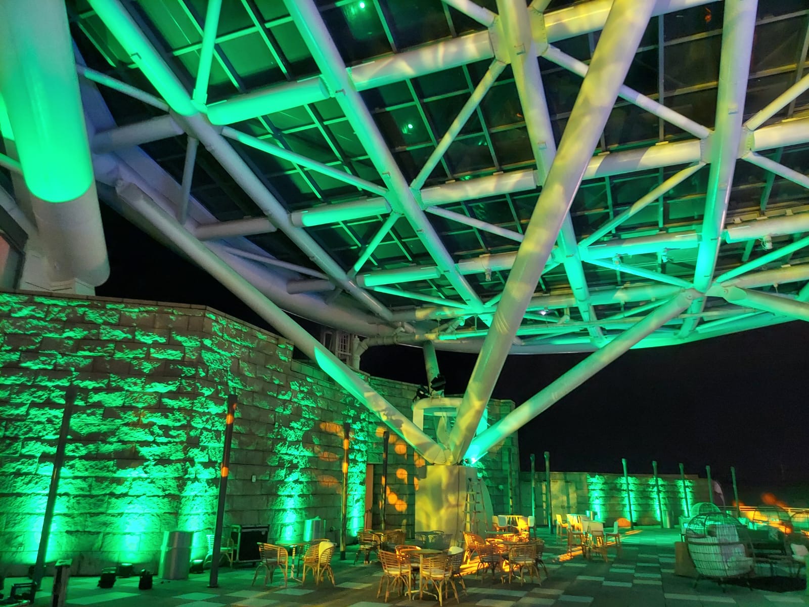 Green architectural lighting illuminates an outdoor terrace and its overhead structure