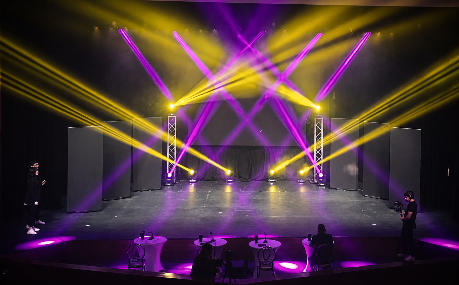 Yellow and purple beams cross above a theater stage